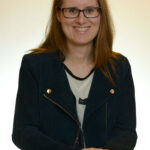 Eine Frau mit Brille und schwarzer Jacke, die in die Kamera schaut