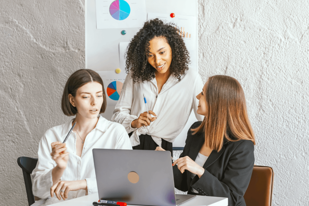 Drei Frauen sitzen zusammen im Büro, schauen auf einen Laptop. Eine erklärt etwas, die anderen hören zu.