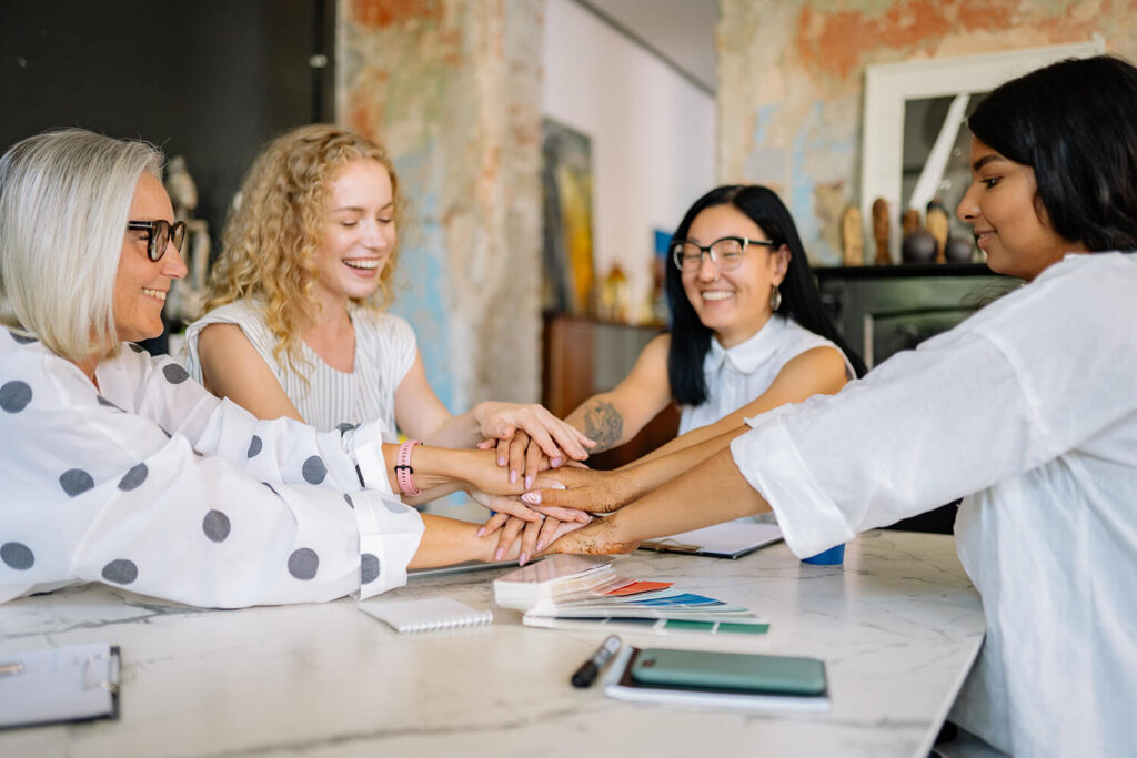 Vier Frauen legen ihre Hände übereinander und symbolisieren Teamarbeit.