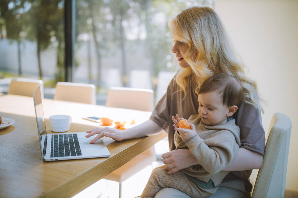 Mutter arbeitet von zu Hause mit Baby auf dem Schoß.